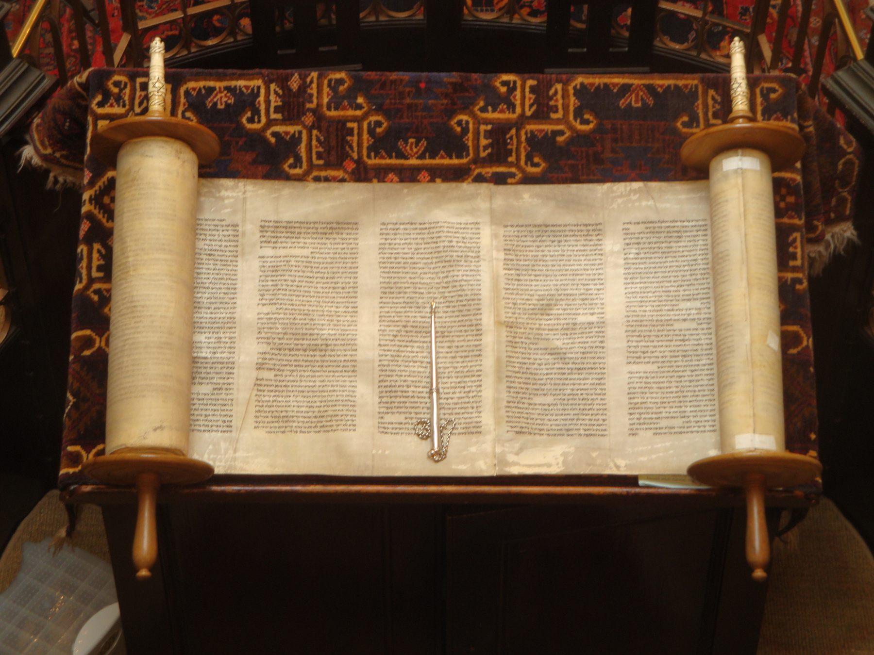 An open Torah scroll with a silver yad resting on the parchment